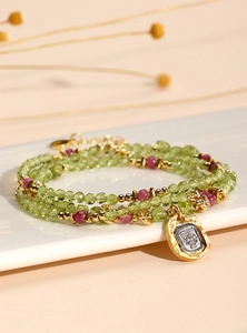 Detail of beaded peridot necklace with a vintage gold relief pendant on ceramic surface