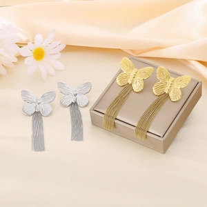 Close-up of elegant gold and silver butterfly tassel earrings on champagne silk fabric