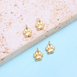Golden stainless steel cat paw pendants set with tiny white zircons on stone surface