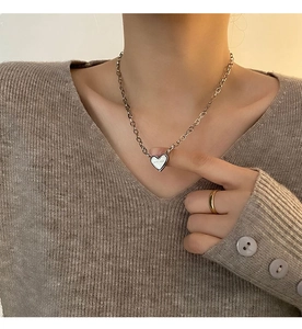 Detailed view of elegant silver heart necklace and gold band ring on a knit sweater