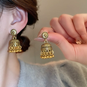 Close-up of vintage golden bell earring with intricate hollow carvings and beaded fringe