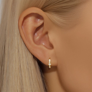 Close-up of model wearing gold hoop earrings with three inlaid white zircon stones