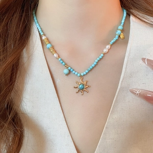Détail du collier en turquoise et perles avec pendentif soleil doré sur le cou