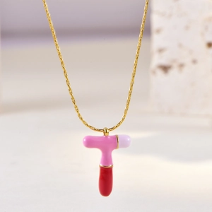 Macro detail of T-shaped gold necklace pendant with pink and white enamel drip finish
