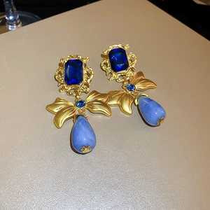 Dettaglio di orecchini vintage dorati con gemme blu rettangolari e pendenti a goccia