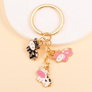 Detail of golden keychain featuring three cute enamel cow charms in pink and black spots
