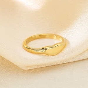 Macro detail of minimalist heart ring in gold finish on luxurious champagne silk background