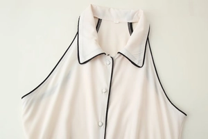 Détail d'une robe chemise beige sans manches avec col à revers et liseré noir contrasté