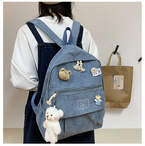 Detalle de mochila de pana azul claro con parche de oso y colgante de peluche