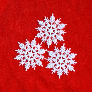 Three white plastic snowflake ornaments displayed on a festive red velvet background
