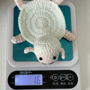 Handmade crochet lamb coaster in cream white and pink being weighed on a digital scale