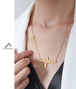Detail of gold heartbeat pendant and heart charm necklace worn with white suit