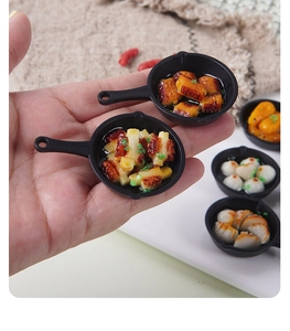 Miniature black frying pan food model with dumplings and stir-fry dishes held on fingertips