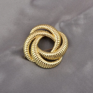 Detailed macro view of a golden twisted rope knot brooch with metallic texture on fabric