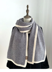 Close-up of a grey knitted scarf with beige trim and small brown woven brand label