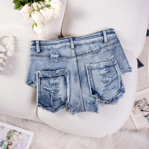 Dettaglio di pantaloncini in denim a vita alta con orlo sfrangiato su divano bianco