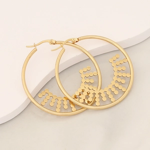Close-up of gold hoop earrings with geometric sun pattern on a white platform