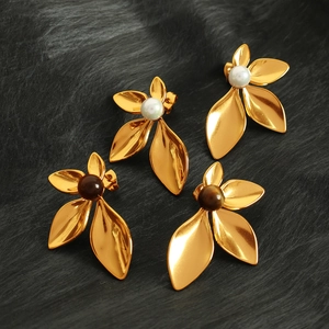 Elegant gold flower earrings with natural stone and pearl centers on a black plush background