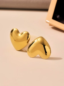 Detail shot of heart-shaped gold earrings on a seashell, highlighting polished mirror finish