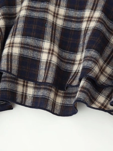 Detailed close-up of blue and beige plaid fabric texture with wavy hem and overlock stitching