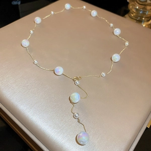 Detailed view of Y-shaped gold necklace with iridescent white pearls on beige leather