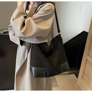 Close-up of black suede tote bag with leather corner reinforcement and white topstitching