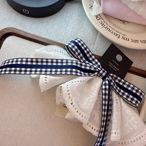 Close-up of white lace bow hair clip with blue gingham ribbon on a display card