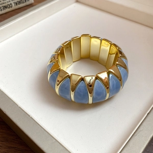 Detailed shot of chunky gold elastic bracelet featuring sky blue marbled resin inserts