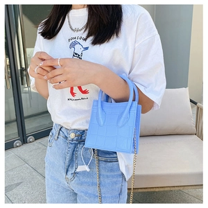 Close-up of light blue crocodile pattern handbag with gold chain strap held by a model