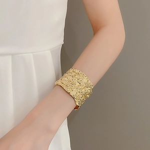 Detailed close-up of wide golden textured metal cuff bracelet with hammered pleated finish
