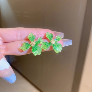 Nahaufnahme von grünen Blumenohrringen mit Goldakzenten, von Hand gehalten