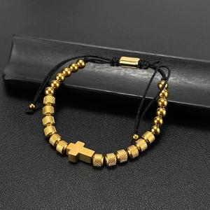Detailed view of golden cross pendant and textured beads on adjustable woven bracelet