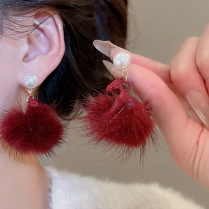 Close-up of red pompom and pearl drop earring with horse accent worn by a model