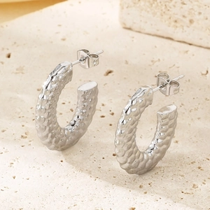 Macro shot of silver C-shaped earrings with irregular hammered texture on beige stone