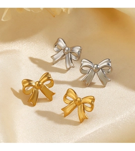 Flat lay of gold and silver metallic bow earrings on a smooth beige silk background