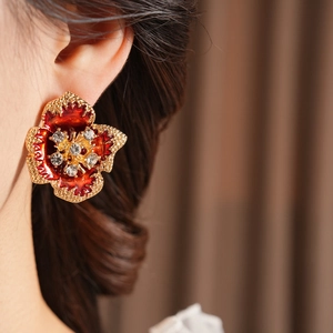 Close-up of red enamel flower earrings with gold edges and crystal flower center