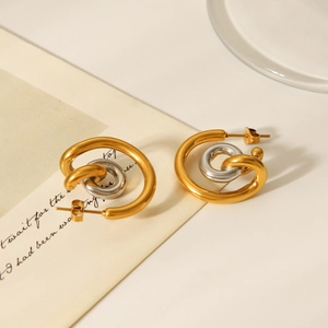 Detail of interlocking gold and silver curved hoop earrings on a minimalist background