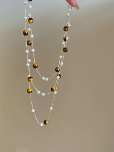 Detail of layered necklace featuring brown tiger eye beads and white pearls on a gold chain