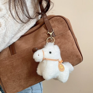 Ciondolo a forma di pony in peluche bianco appeso a una borsa a tracolla in pelle scamosciata