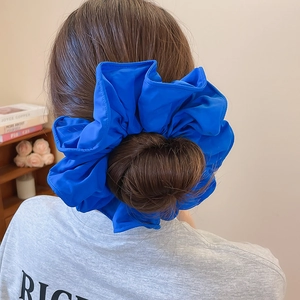 Chouchou géant en tissu bleu au design froufrou porté sur un chignon élégant
