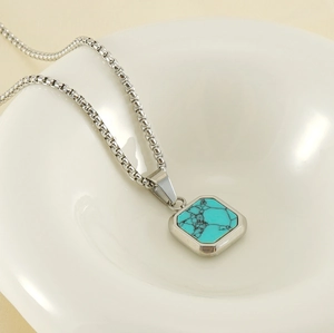 Gros plan d'un collier en acier titane argenté avec un pendentif en turquoise carrée