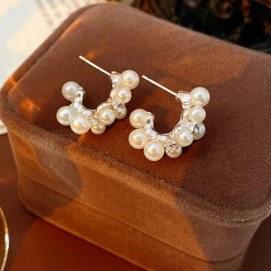Primer plano de pendientes en forma de C con perlas y diamantes en caja de terciopelo marrón