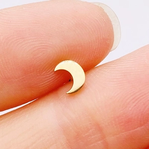 Macro shot of a tiny gold moon-shaped stainless steel cartilage stud on a fingertip