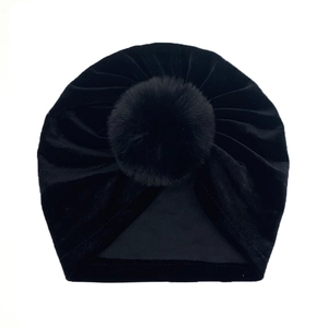 Detailed view of black velvet baby hat with a soft pompom and pleated texture