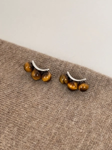 Macro detail of tiger eye stone earrings with three beads on textured brown fabric