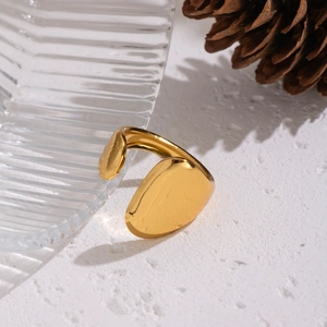 Detail view of a gold geometric open ring on textured surface with decorative pine cone