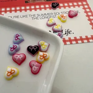 Pastel heart and bow resin nail art charms in candy colors on a ceramic tray