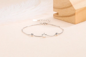 Close-up of silver star pendant and polished round beads on a minimalist chain bracelet