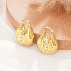 Détail de boucles d'oreilles dorées avec texture losange sur socle en bois