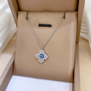 Macro shot of silver four-leaf clover necklace with blue evil eye pendant and zircons